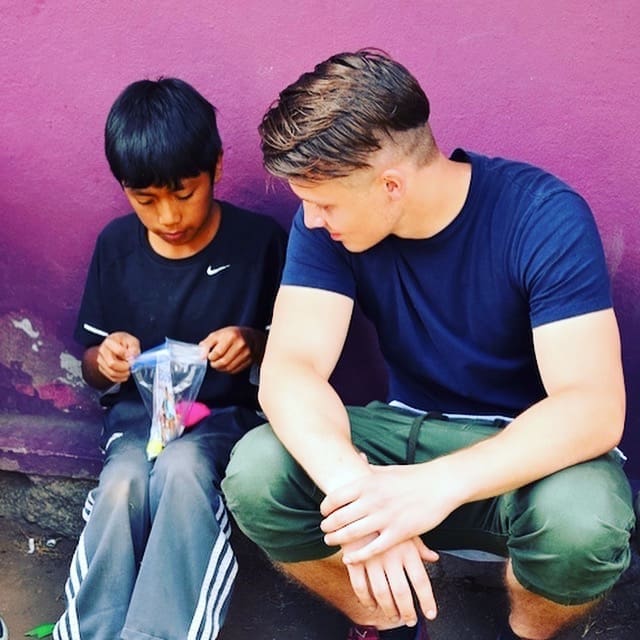 Photo of a young man with a small boy sitting against a wall